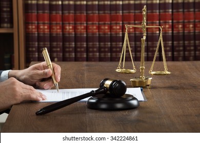 Cropped Image Of Male Judge Writing On Legal Documents At Desk In Courtroom