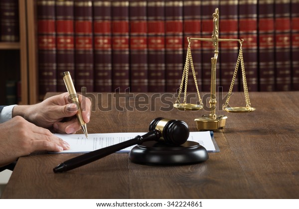 Cropped image of male judge writing on legal\
documents at desk in\
courtroom