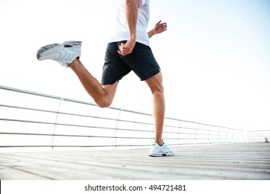 Cropped Image Of Man Athlete Runner's Feet And Shoes Running Along Beach Pier