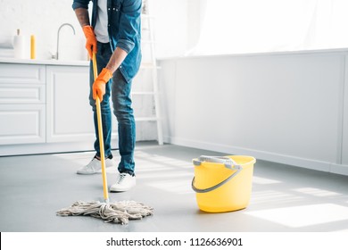 cropped image of man cleaning floor in kitchen with mop