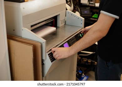 Cropped image man hands using paper cutter machine, guillotine offset. Manufacturing work. Rotate buttons, control panel, display, set up laser level, alignment, leveling stack papers in tray pusher. 