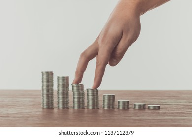 cropped image of man walking with fingers on stacks of coins on table, saving concept