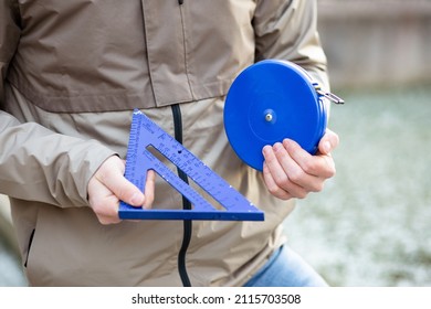 Cropped image of man wearing jacket hands holding blue building special housing measurement tools instruments square and coil roulette. Daylight side view. Blur smooth background