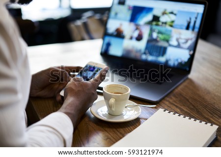 Photo of Cropped image of man's hand holding modern smartphone while sending multimedia files to laptop computer editing before publish with mock up screen connected to free wireless internet in coffee shop
