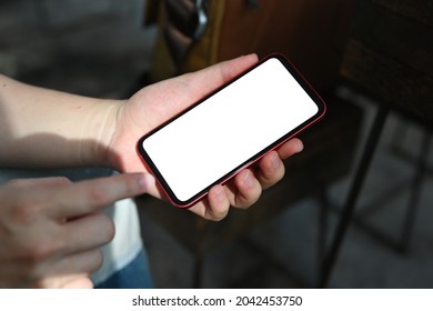 Cropped image of a man's hand using a white screen smartphone over a comfortable living room as a background.