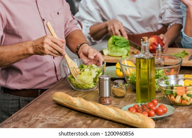 cropped image of mature friends preparing salad for dinner together at home - Shutterstock ID 1200960856