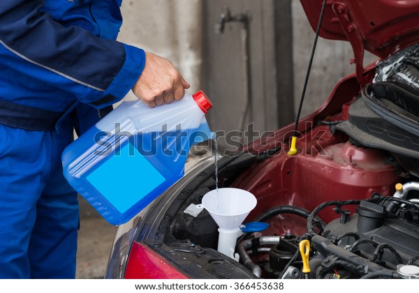 Cropped image of mature serviceman\
pouring windshield washer fluid into car at service\
station