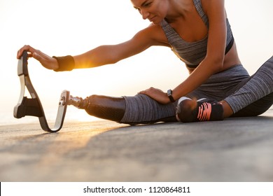 Cropped image of motivated disabled athlete woman with prosthetic leg doing stretching exercises while sitting at the beach - Powered by Shutterstock