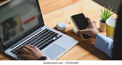 Cropped image of an office woman is charging a smartphone with a wireless charger while typing on a computer laptop.