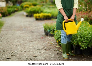 Cropped Image Of Outdoor Flower Shop Worker In Apron And Rubber Boots Holding Watering Pot