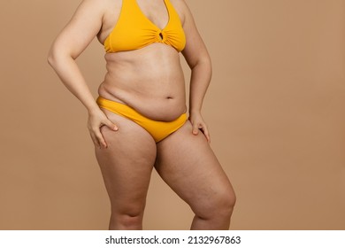 Cropped image of overweight fat naked woman with obesity hips, excess fat in yellow swimsuit. Big size. Holding hips flabs, visceral, cellulite. Self acceptance, body positive, imperfection skin body