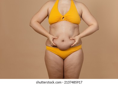 Cropped image of overweight fat naked woman with obesity, excess fat in yellow swimsuit. Adipose. Holding stomach flabs, visceral, cellulite. Self acceptance, body positive, plus size, friable skin