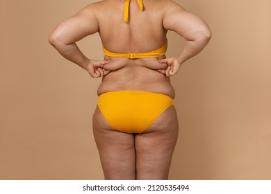 Cropped image of overweight fat woman back with obesity, excess fat in yellow swimsuit. Big size. Holding waist flabs, visceral, cellulite. Varicose veins, imperfection skin puffy body. Liposuction