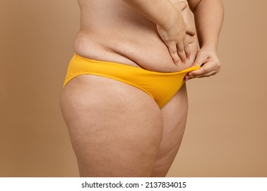 Cropped image of overweight fat woman stomach with obesity, excess fat in yellow swimsuit. Fast weight loss. Holding stomach flabs, hiding tummy cellulite. Sagging flabby skin. Go on unhealthy diet.
