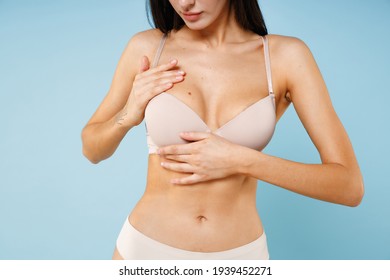 Cropped image of pretty young brunette woman 20s in beige underwear standing put hands on chest breast cancer early diagnostic therapy treatment isolated on pastel blue background, studio portrait