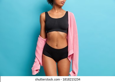 Cropped image of sexy woman with perfect figure dressed in black underwear has flat abdomen isolated on blue background. Sporty female body for your motivation