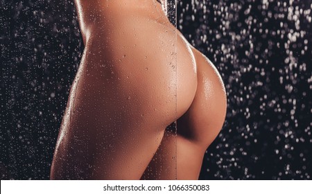Cropped image of sexy woman in shower. Attractive young naked woman under water drops isolated on black background. Close-up of woman's buttocks.