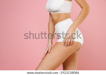 Cropped image side view of alluring seductive young woman wearing white underwear with fit sexy body standing posing hold hand on hips legs isolated on pastel pink colour background, studio portrait