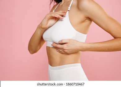Cropped image side view of young brunette woman 20s in white brassiere underwear put hand on chest breast cancer early diagnostic therapy treatment isolated on pastel pink background, studio portrait