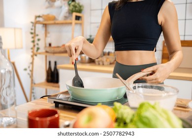 A cropped image of a slim, athlete woman in workout attire cooking in the kitchen, making pancakes for her breakfast. healthy lifestyle, domestic life, home cooking - Powered by Shutterstock