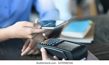 Cropped image of smart man's hands holding a smartphone and doing a payment by using a NFC technology at the Credit card reader that putting on cafe payment counter. Technology and Payment concept.