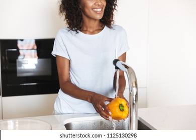 Cropped image of a smiling afro american woman washing vegetables to make a salad at the kitchen - Powered by Shutterstock