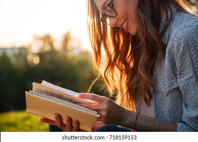 Cropped image of smiling brunette woman in eyeglasses reading book in park - Shutterstock ID 718159153