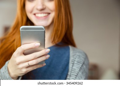 Cropped image of a smiling redhead woman using smartphone