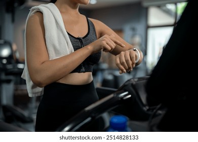 A cropped image of a sporty woman in sportswear is setting her smartwatch while she is on a treadmill running machine in a fitness gym. an image with a copy space. fitness, exercise, workout, training - Powered by Shutterstock