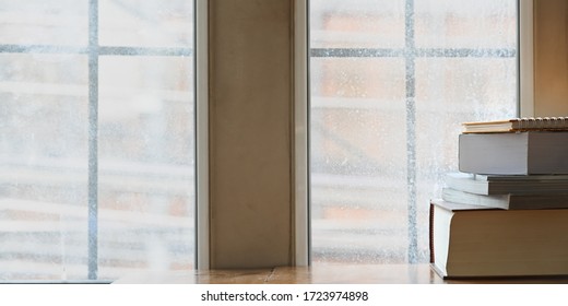 Cropped image stack of books putting on wooden table over window sill with snowing outside as background. Concept of relaxation time on winter.