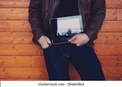 Cropped Image With Stylish Young Man Holding Digital Tablet With A Blank Screen, Hipster Student With Touch Pad Standing On Wooden Background, Man's Hands Holding Black Tablet With Copy Space Area