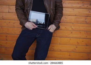 Cropped Image With Stylish Young Man Holding Digital Tablet With A Blank Screen, Hipster Student With Touch Pad Standing On Wooden Background, Man's Hands Holding Black Tablet With Copy Space Area