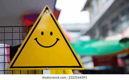 Cropped image of triangle road sign with a smiley face with blurred market road background. Positive thinking, mental health assessment , world mental health day concept