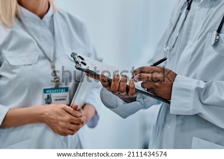 Cropped image of two doctors writing information on forms. Background.