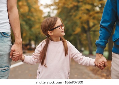 Cropped Image Of Two Gay Parents With Their Adopted Daughter Holding Hands And Walking In Park Together. Happy LGBT Family Concept.