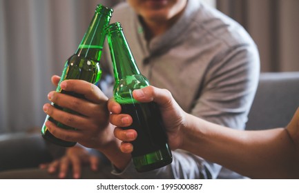 Cropped image of two men clinking bottles of beer together while sitting on sofa. - Powered by Shutterstock