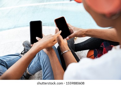 Cropped image of two stylish african american girls in trendy streetwear sitting on playdround with basketball and smartphones - Shutterstock ID 1559880608