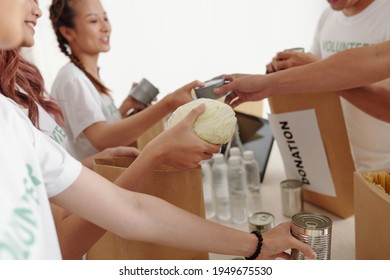 Cropped image of voluneers packing waterr, canned food and vegetables in paper packages for people who lost homes after hurricane or flood