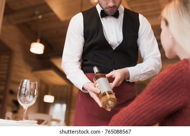 Cropped image of waiter proposing bottle of white wine to the customer