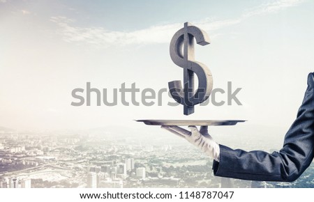 Cropped image of waiter's hand in glove presenting stone dollar symbol on metal tray with cityscape view on background. 3D rendering.
