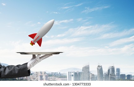 Cropped image of waitress's hand in white glove presenting flying missile on metal tray with cityscape view on background. - Powered by Shutterstock