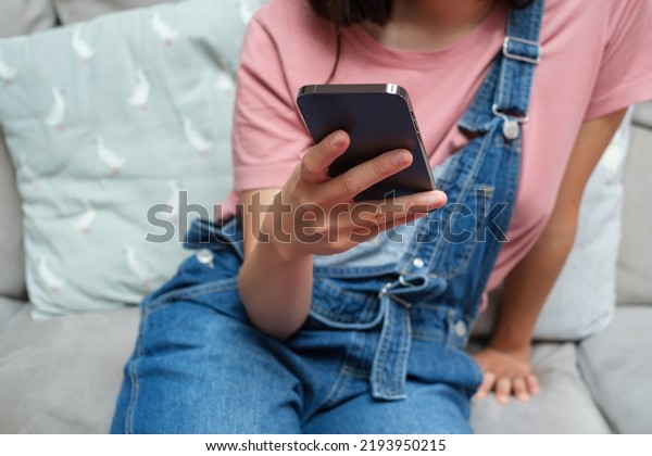 Cropped\
Image Of Woman with Bib Overalls using\
phone