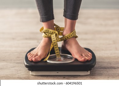 Cropped image of woman feet standing on weigh scales, on gray background. Legs winded with a tape measure