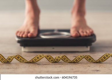 Cropped image of woman feet standing on weigh scales, on gray background. A tape measure in the foreground - Shutterstock ID 604196735