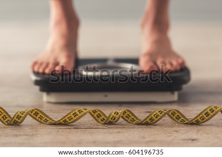 Cropped image of woman feet standing on weigh scales, on gray background. A tape measure in the foreground