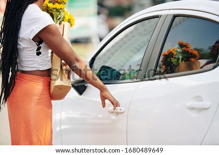 Cropped image of woman with grocery bag and bouquet of sunflowers opening car door