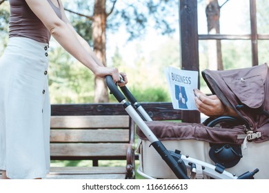 Cropped Image Of Woman Holding Baby Carriage In Park, Someone Holding Business Newspaper In Baby Carriage