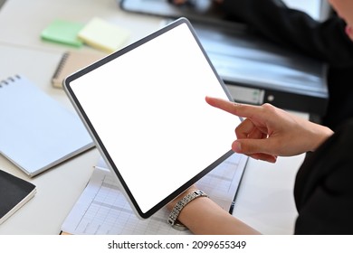 Cropped Image Of A Woman Holding A White Blank Screen Digital Tablet At The Cluttered Working Desk.