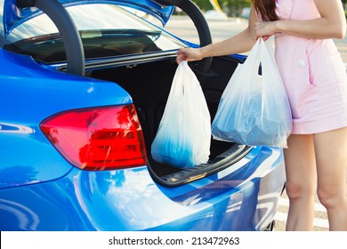 Cropped Image Of Woman Putting Shopping Bags Inside Trunk Of Her Blue Car, On A Mall, Store, Supermarket Parking Lot