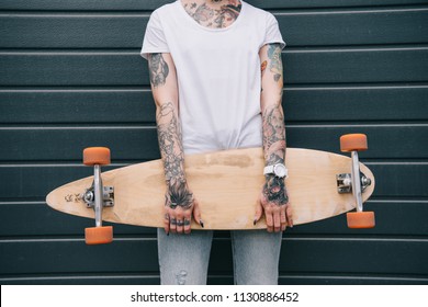 Cropped Image Of Woman With Tattoos Holding Skateboard Against Black Wall 